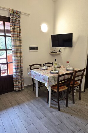 A dining area with a table set for four, chairs, a television mounted on the wall, and a window with curtains.