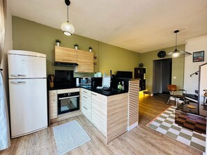 A compact kitchen with a refrigerator, oven, microwave, and a coffee machine. There is a wooden cabinet above the counter and a small rug on the floor. - - Casa Di Mare - Beachfront (Borgo)