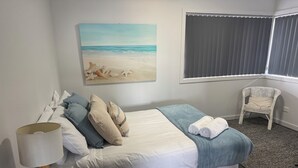 A neatly made bed with a blue and white bedspread, a white lamp, and a painting of a beach scene on the wall. - Conveniently located in the centre of town and close to the beaches (Bridport)