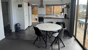 A modern kitchen with a large island, a dining area with a round table and chairs, and a view of the outdoor deck. - Conveniently located in the centre of town and close to the beaches (Bridport)
