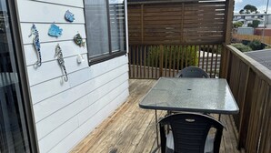 A wooden deck with a table and chairs, a white exterior wall with decorative fish, and a wooden fence. - Conveniently located in the centre of town and close to the beaches (Bridport)