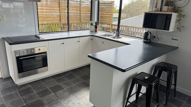 A modern kitchen with a central island, white cabinetry, a built-in oven, and a large window overlooking a wooden deck. - Conveniently located in the centre of town and close to the beaches (Bridport)