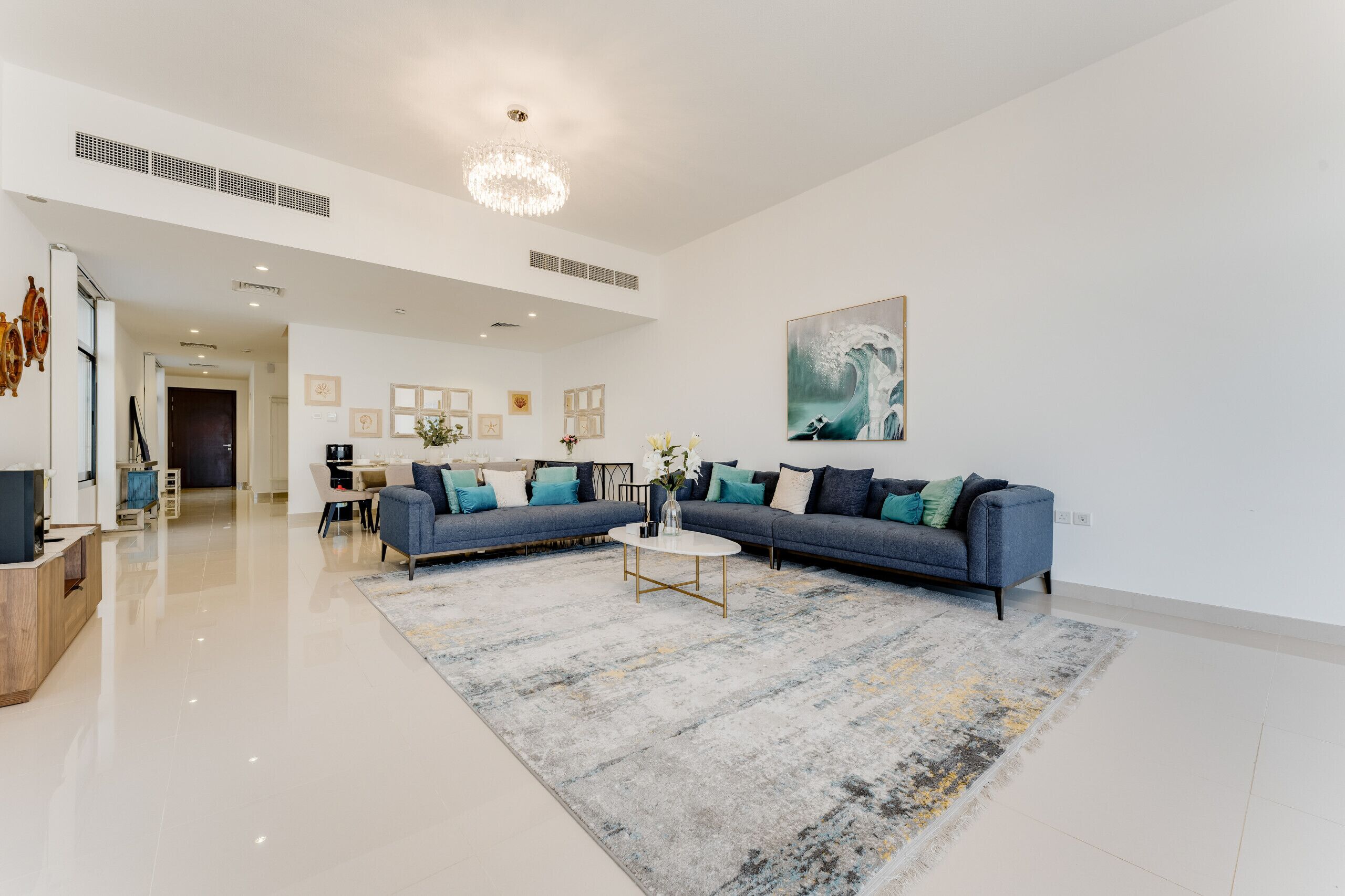 A spacious living room with a large blue sofa, a round coffee table, and a modern chandelier.