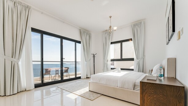 Un dormitorio moderno con una cama grande, una mesita de noche de madera y vistas al mar a través de ventanales.