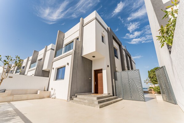 A modern two-story house with a minimalist design, featuring a large glass window, a wooden door, and a concrete staircase leading to the entrance.
