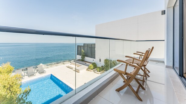 Ein moderner Balkon mit Pool, Holzstühlen und Meerblick.