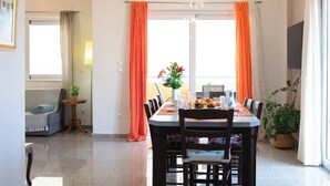 Een eetruimte met een tafel voor zes personen, omringd door stoelen, een kroonluchter en een raam met oranje gordijnen.