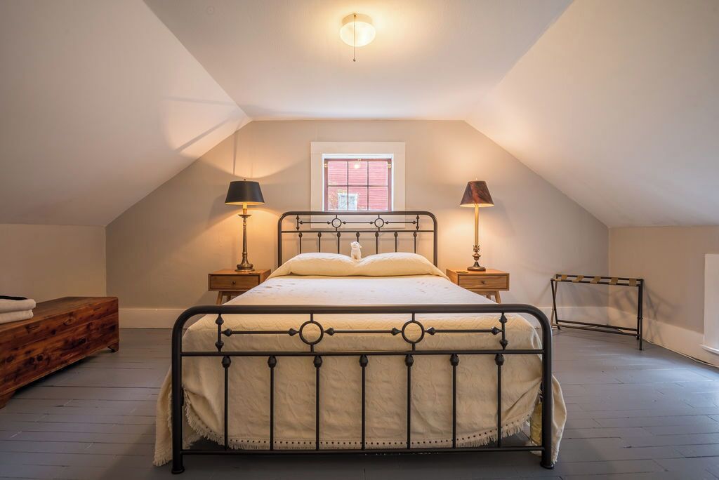 A bedroom with a bed, bedside lamps, a window, and a wooden dresser.
