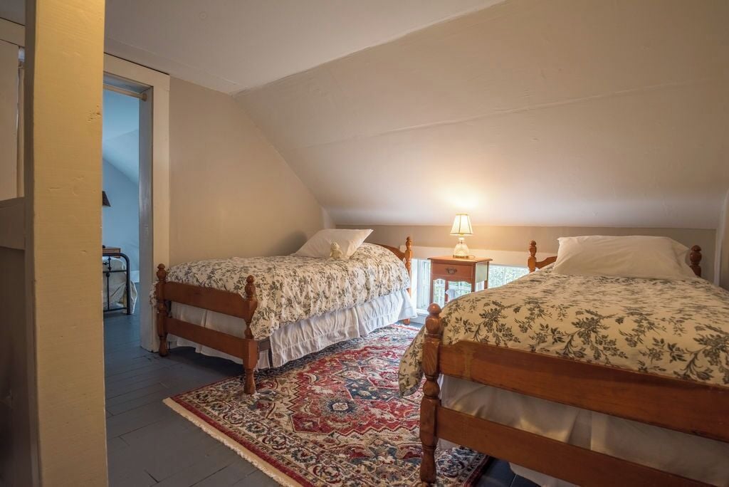 Dos camas de madera con ropa de cama floral en una habitación con techo inclinado y alfombra estampada.