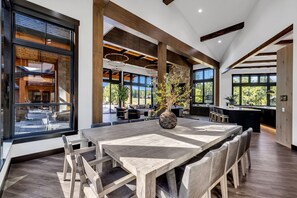 A spacious dining area with a large wooden table, modern pendant lighting, and a stone fireplace.
