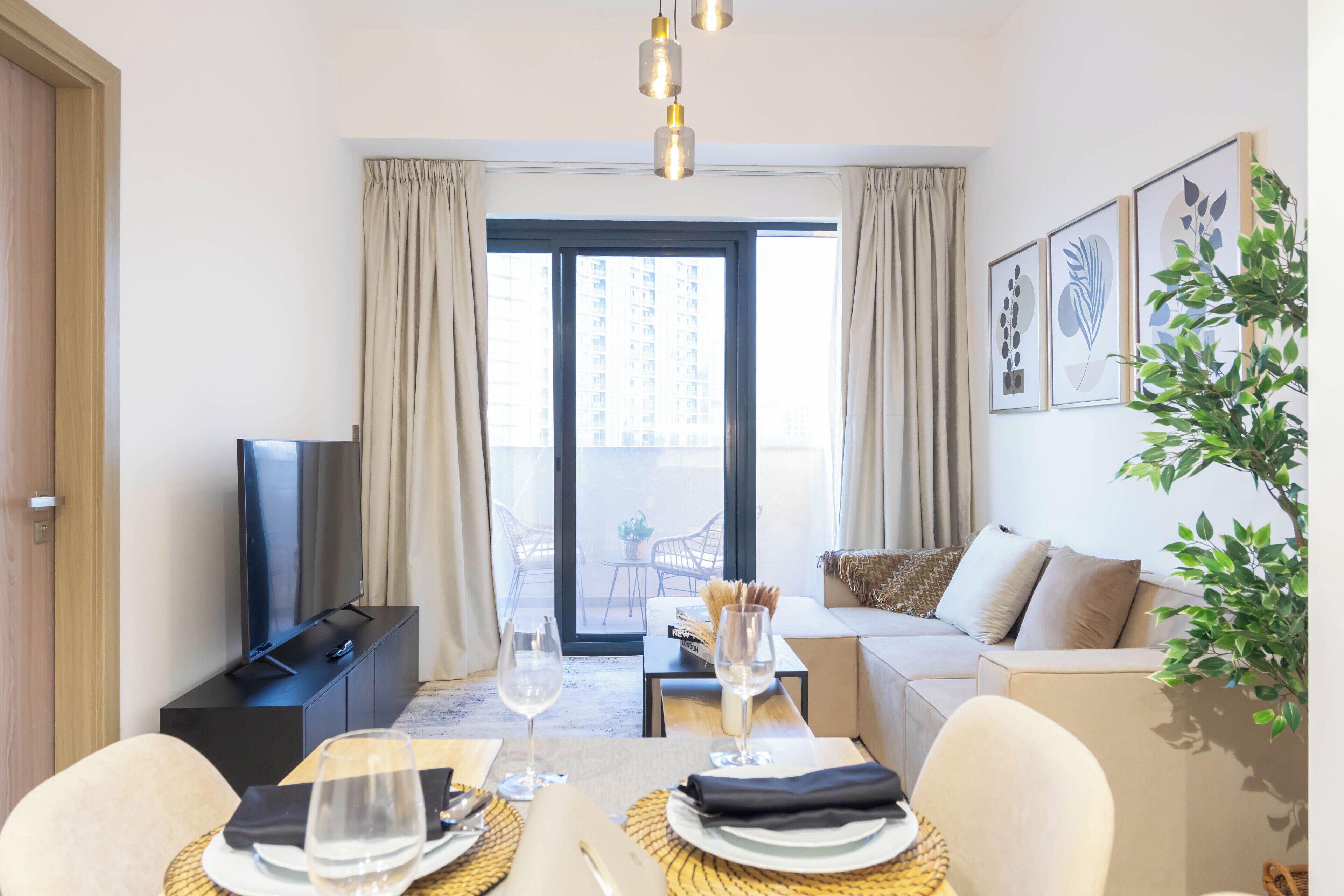Habitación de hotel moderna con comedor, sofá, televisión y balcón con vistas a la ciudad.