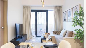 Habitación de hotel moderna con comedor, sofá, televisión y balcón con vistas a la ciudad.
