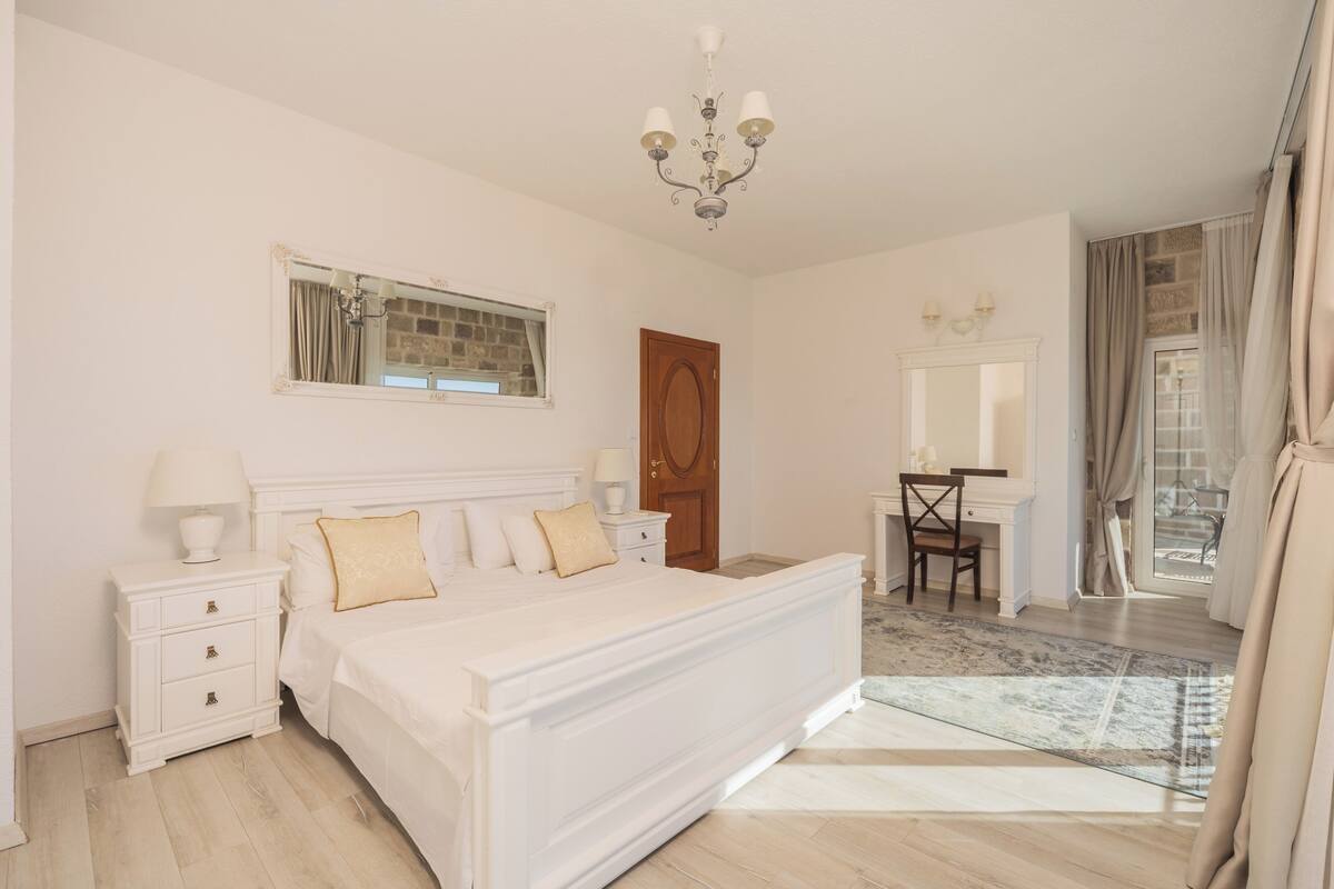 A bedroom with a large bed, a nightstand, a dresser, a desk, and a chair.