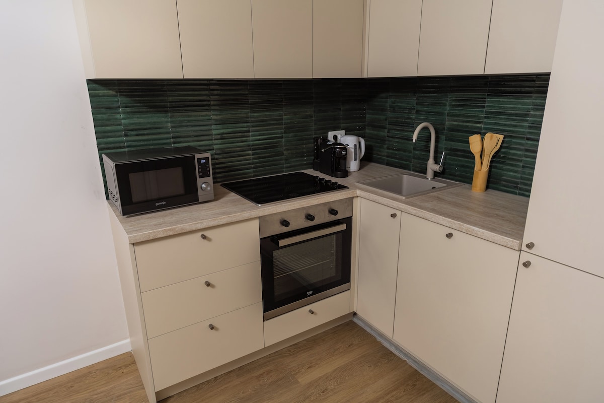 A compact kitchen with a microwave, kettle, sink, and oven.