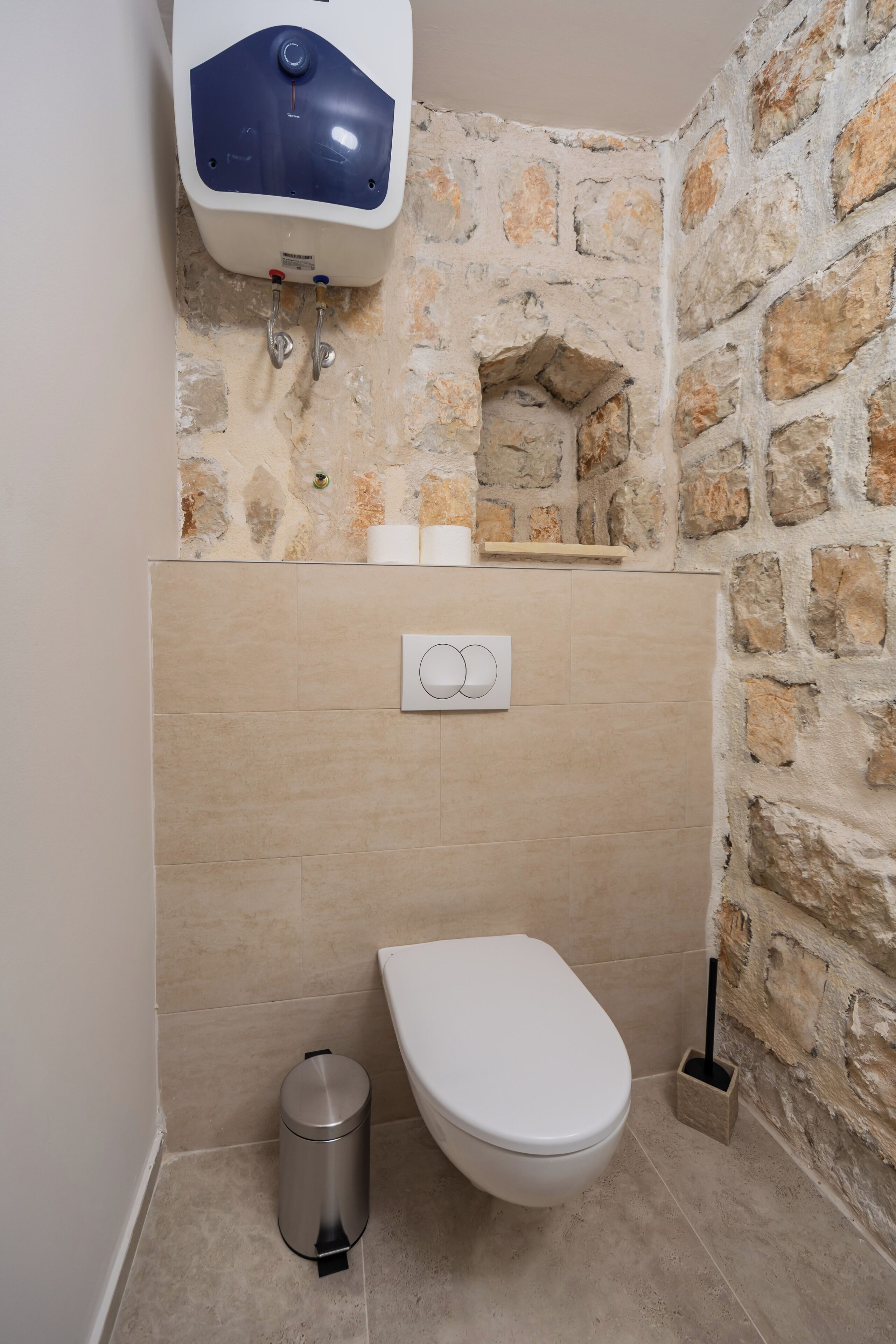 A bathroom with a stone wall, a toilet, a bidet, and a trash bin.
