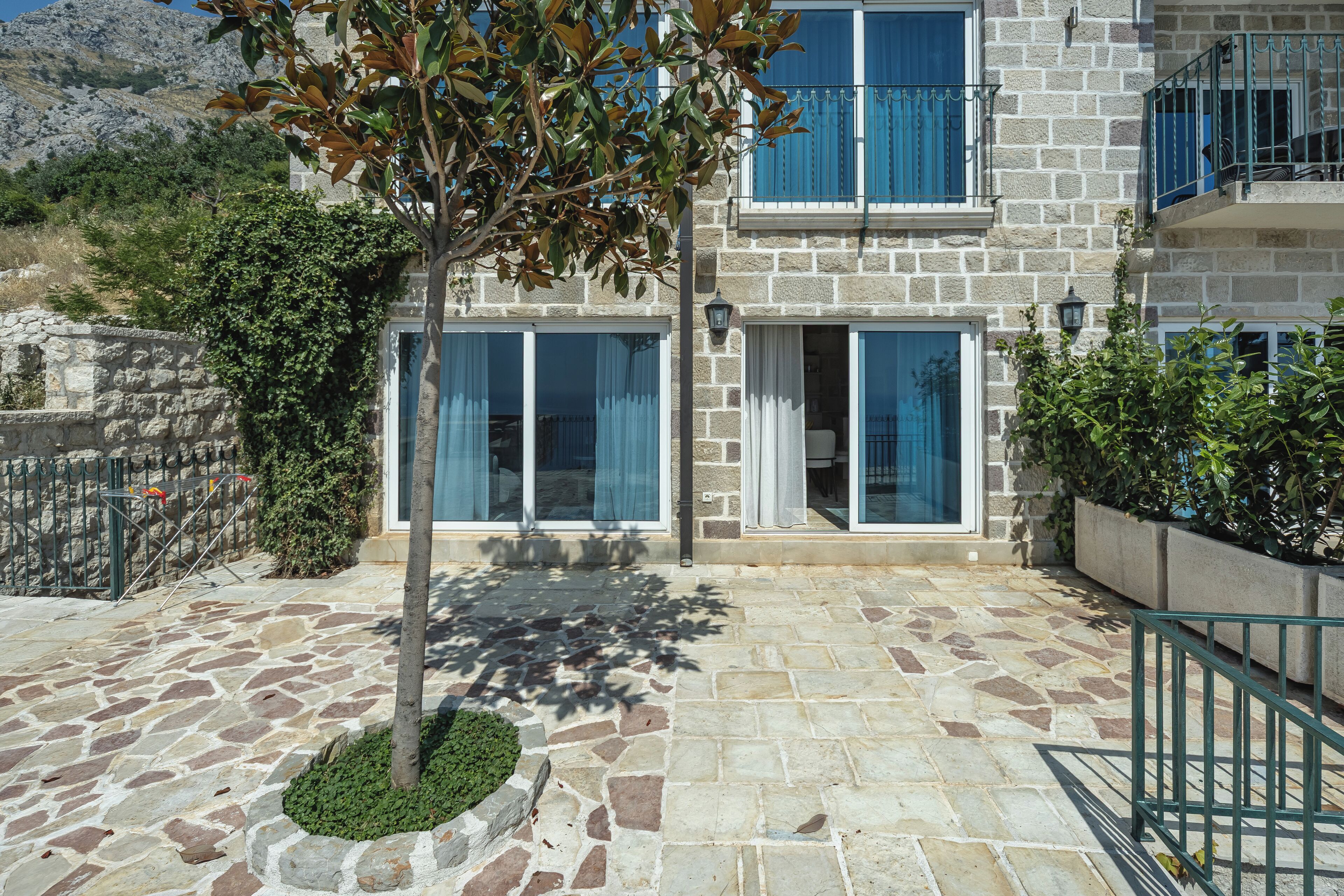 A stone building with a balcony, a tree, and a stone-paved courtyard.