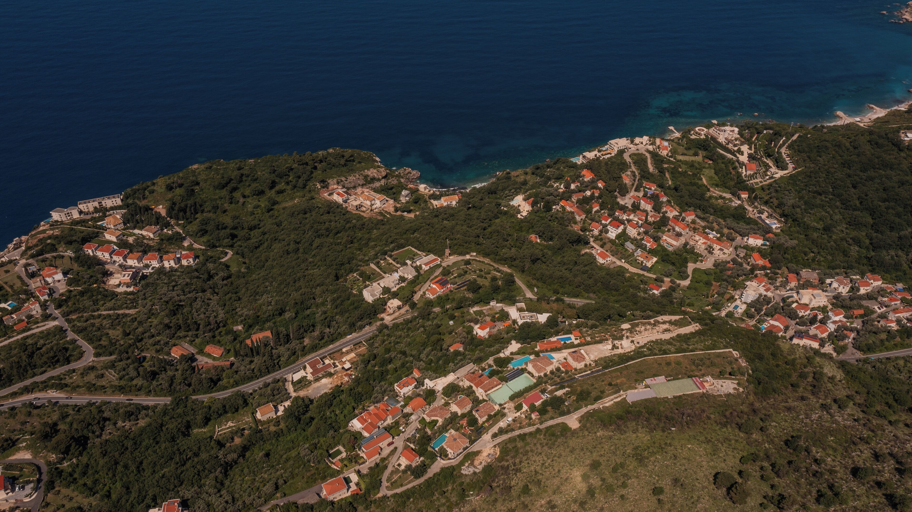 An aerial view of a coastal town with dense housing, roads, and a coastline.