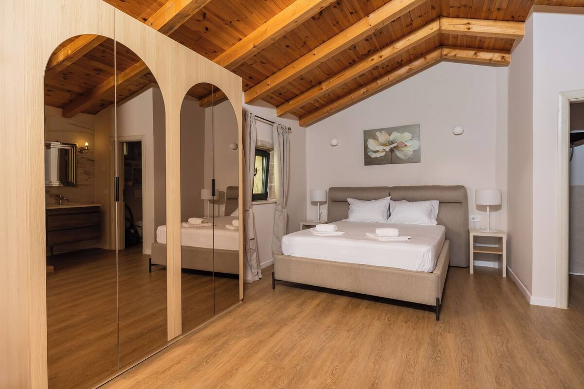 A bedroom with a large bed, wooden ceiling beams, a mirror, and a painting on the wall.