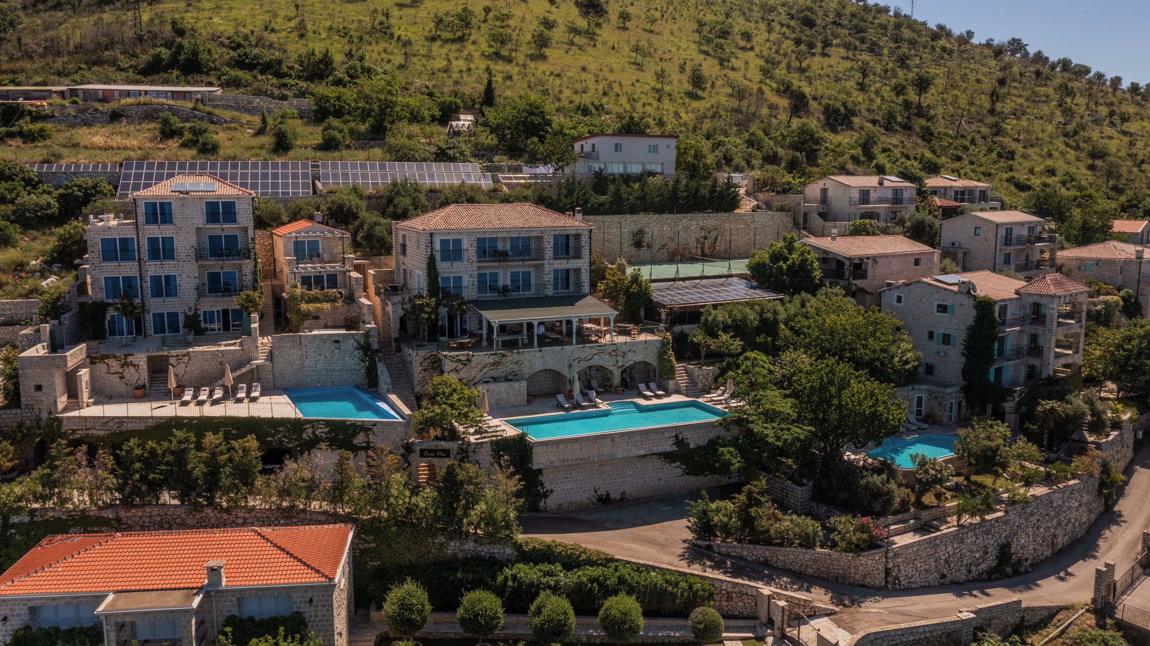 A coastal resort with multiple buildings, a swimming pool, and a hillside backdrop.
