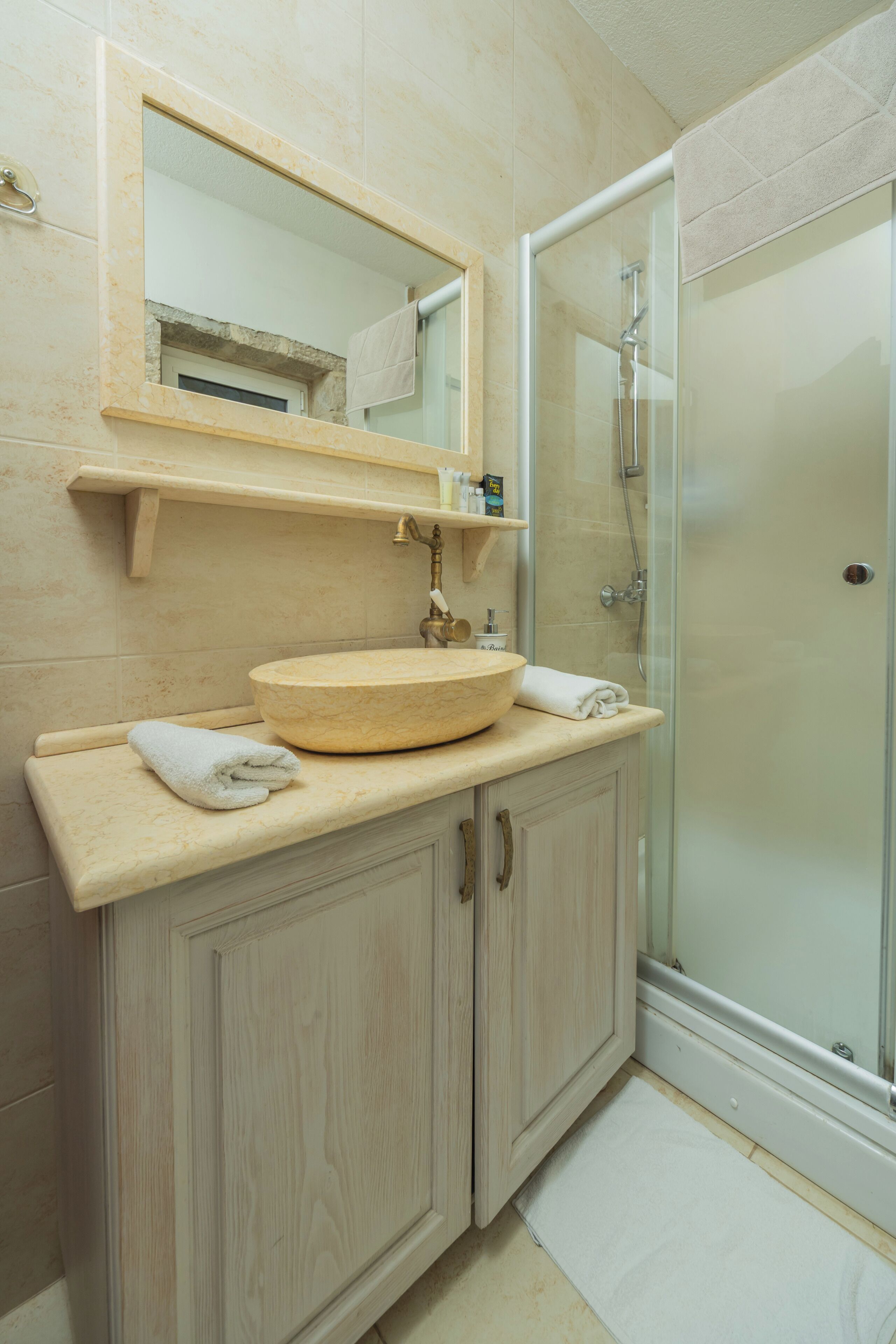 A bathroom with a wooden vanity, a round sink, a mirror, and a glass shower enclosure.