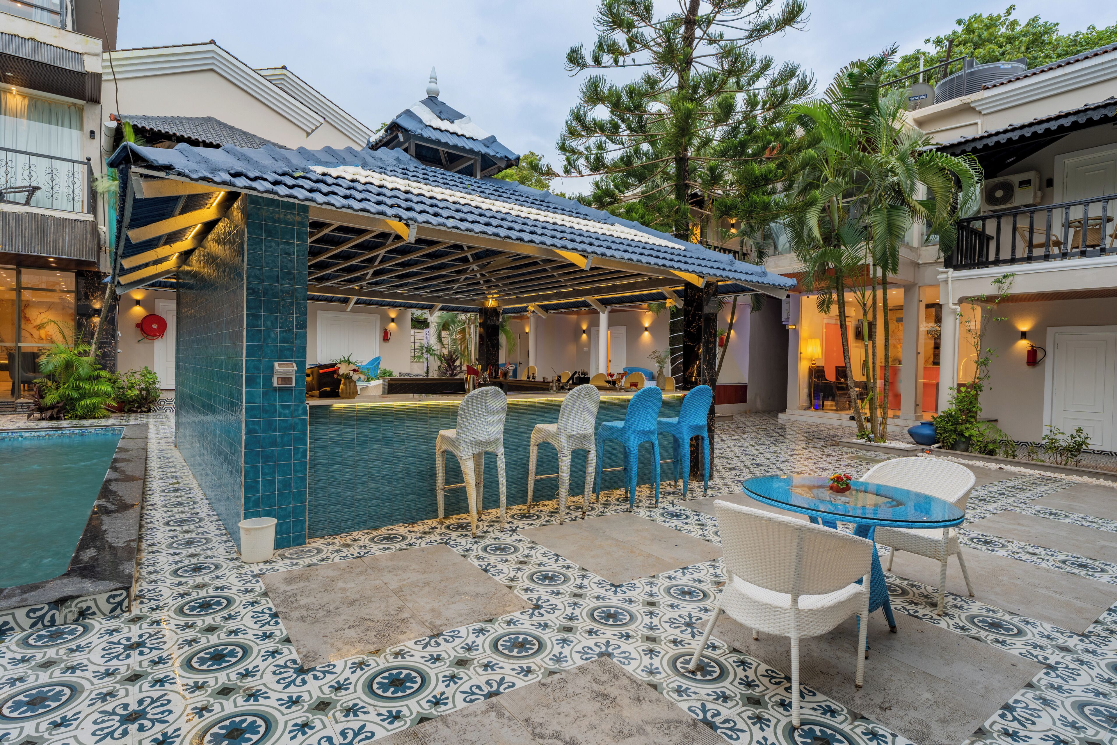 Et poolområde med flisegulv, et overdækket loungeområde med stole og en bar.