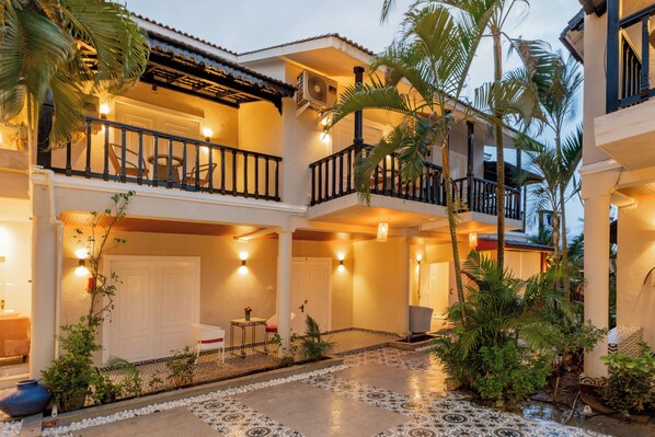 A hotel with a courtyard featuring a tiled floor, palm trees, and a balcony with a railing.