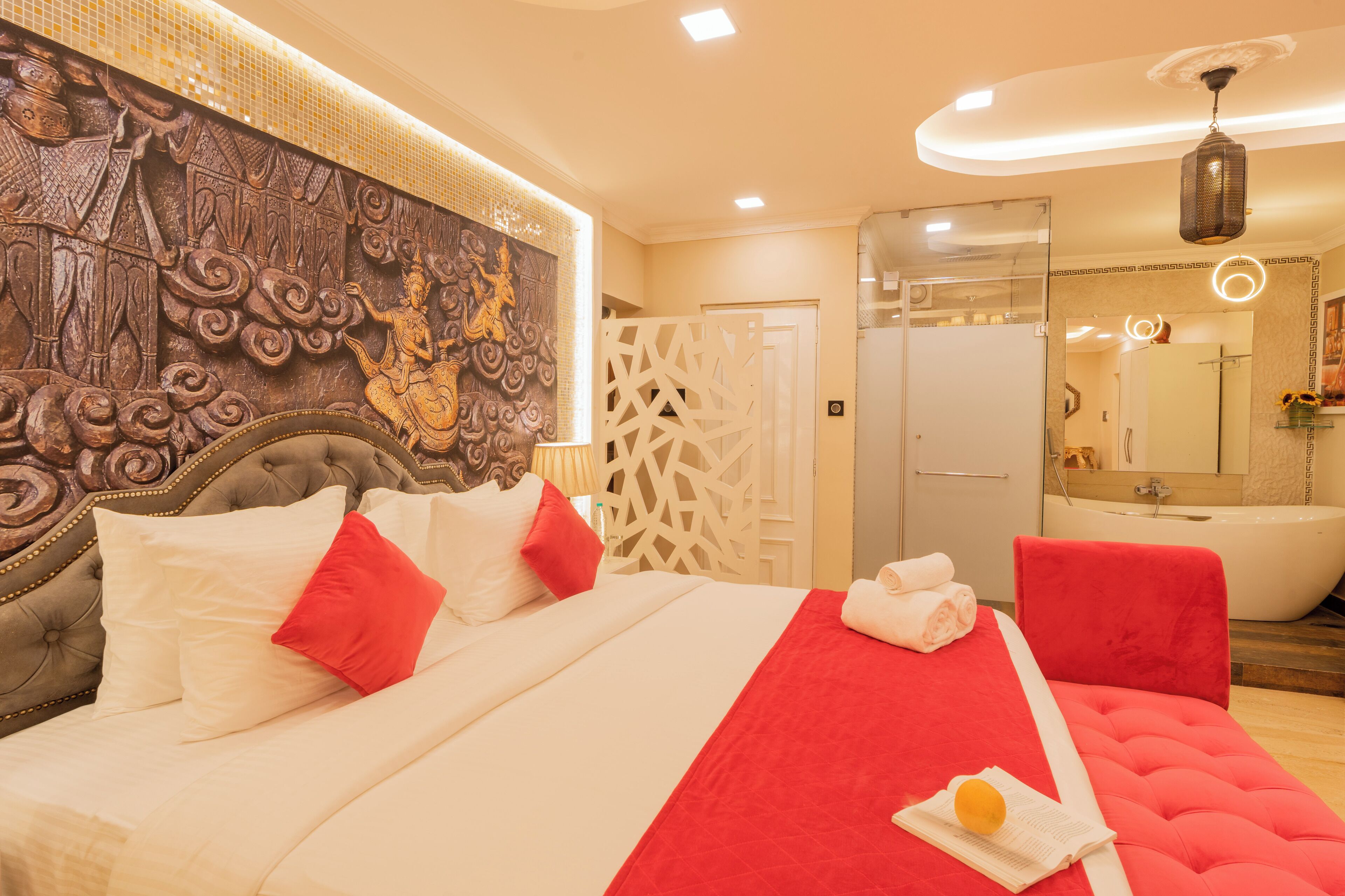 A hotel room with a large bed, a red accent wall, a decorative headboard, a bathtub, and a shower area.