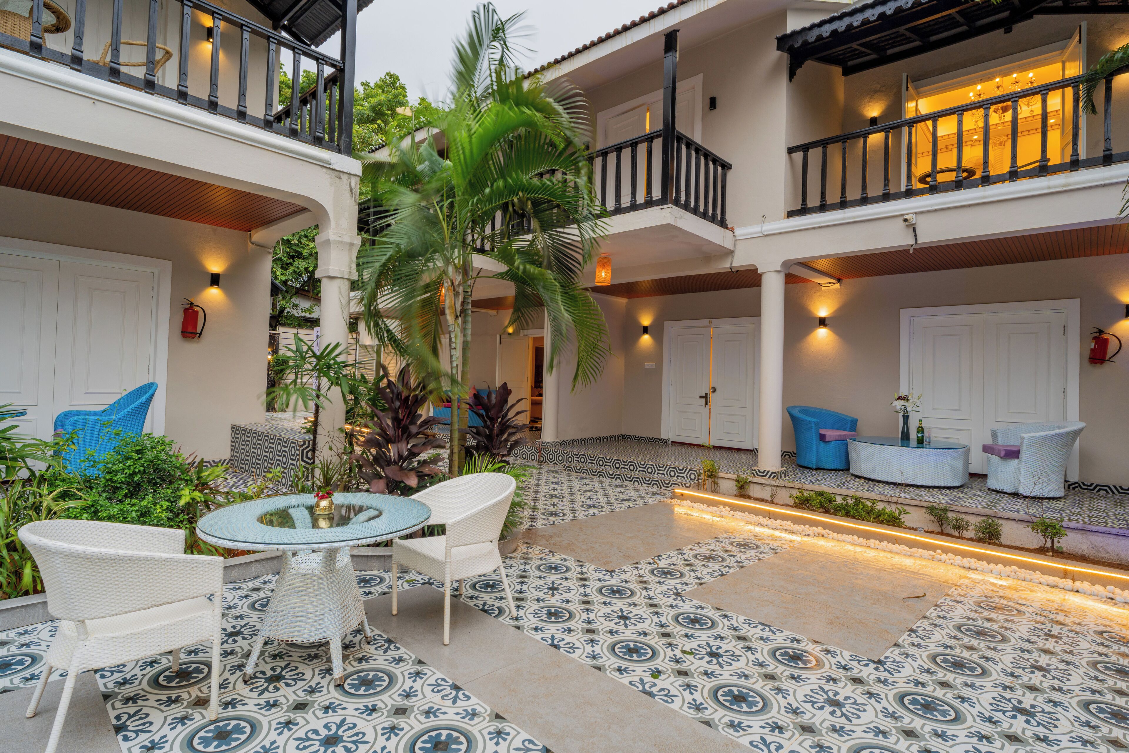 A courtyard with a tiled floor, white wicker furniture, and a palm tree.