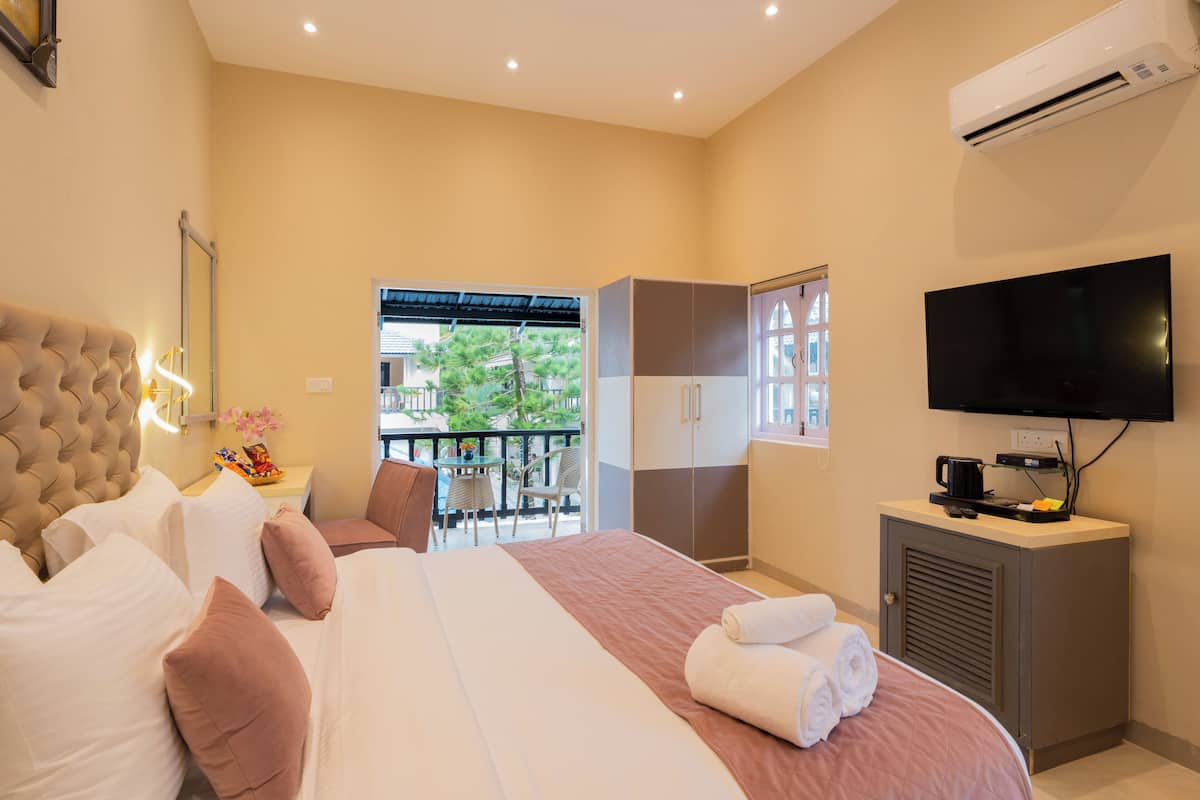 Ein Hotelzimmer mit einem großen Bett, einem Fernseher, einem Kleiderschrank und einem Balkon mit Blick auf Grünflächen.