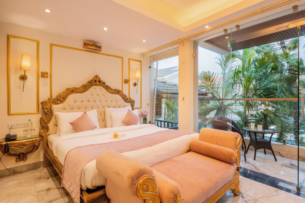 Ein luxuriöses Schlafzimmer mit einem großen Bett, einer Liege und einem Balkon mit tropischen Pflanzen.
