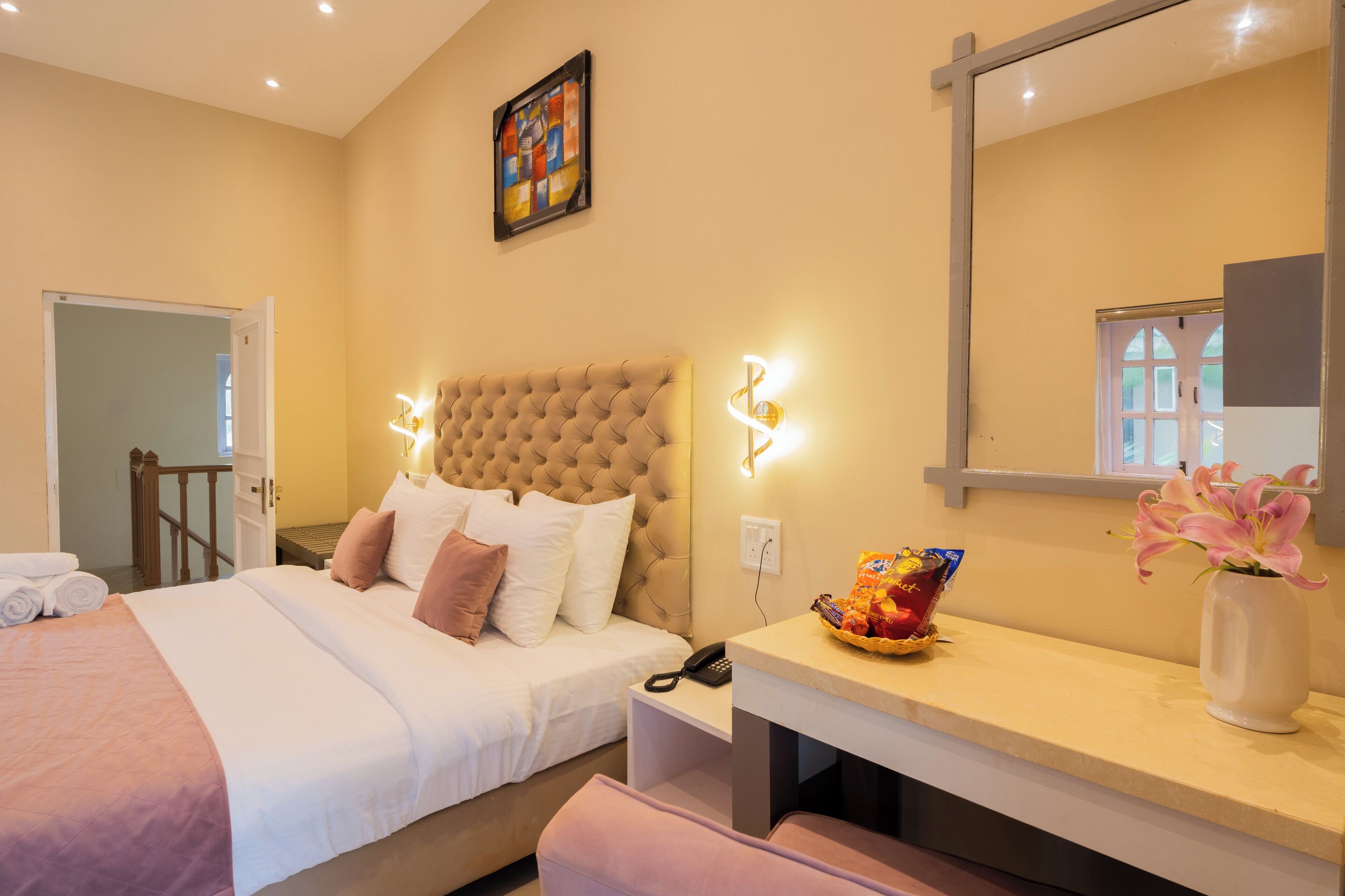 Hotelkamer met een groot bed, nachtkastje met een lamp, een spiegel en een raam met uitzicht op gebouwen.