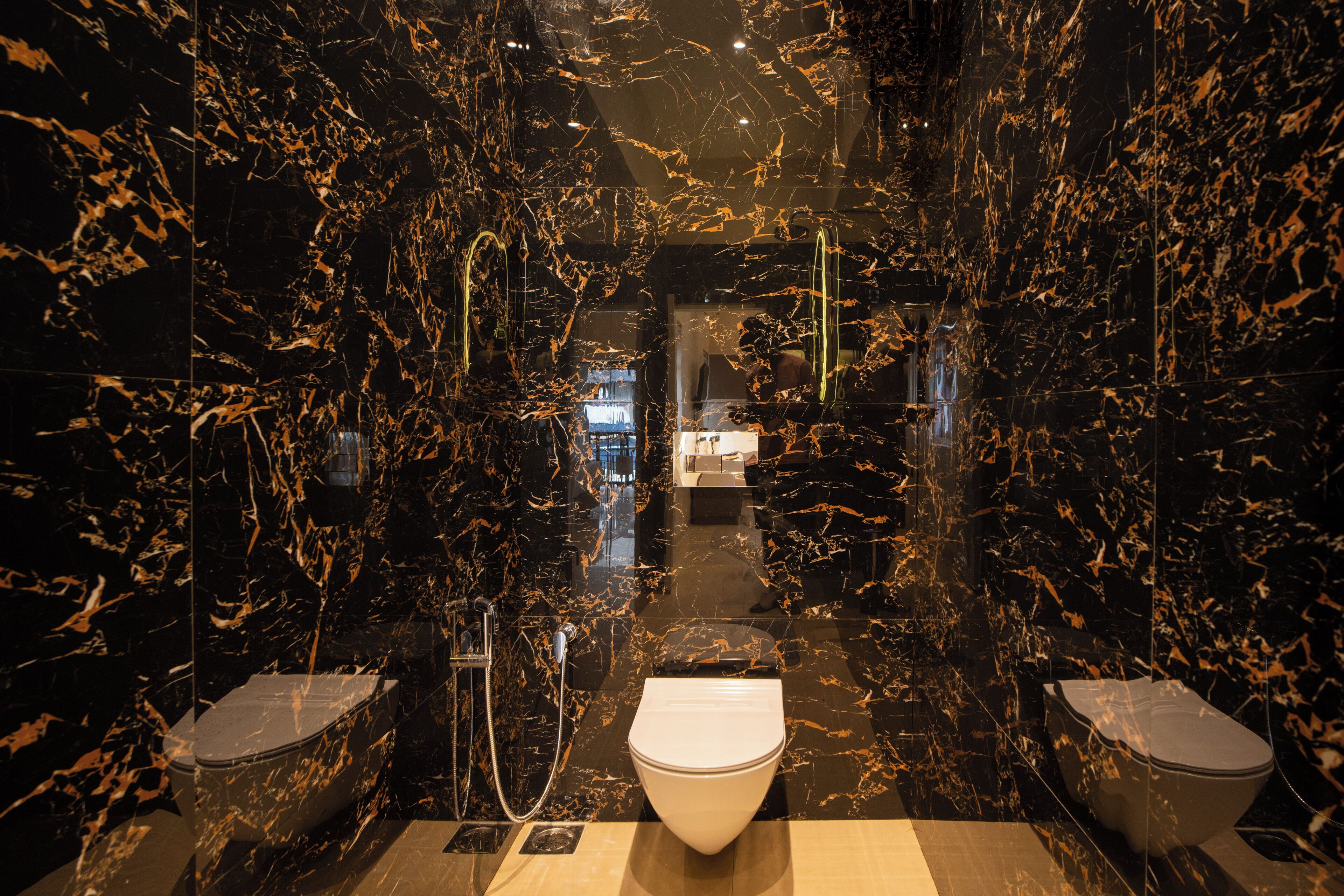 A modern bathroom with black marble walls and floors, a central white toilet, and two additional toilets on either side.