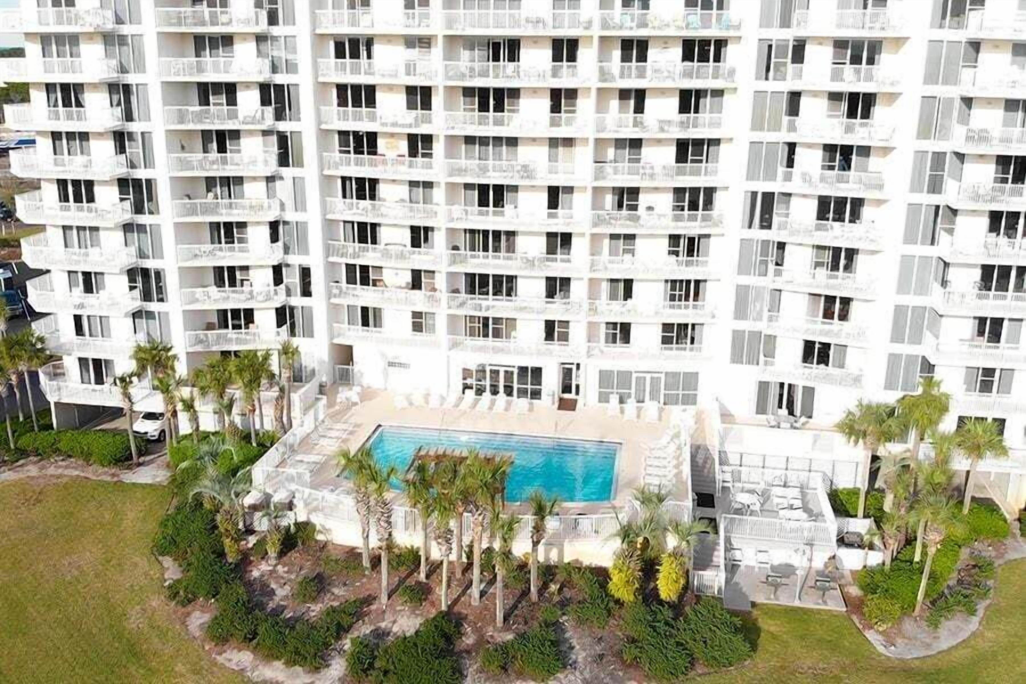Un edificio alto con varios balcones y una piscina rodeada de palmeras.