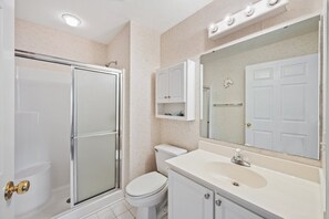 A bathroom with a glass-enclosed shower, a toilet, a sink with a mirror above it, and a cabinet with a towel rack.