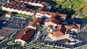 Vista aérea de un complejo residencial con varios edificios, un estacionamiento y una cancha de tenis.