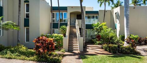 A modern building with a central staircase, surrounded by palm trees and well-maintained gardens.
