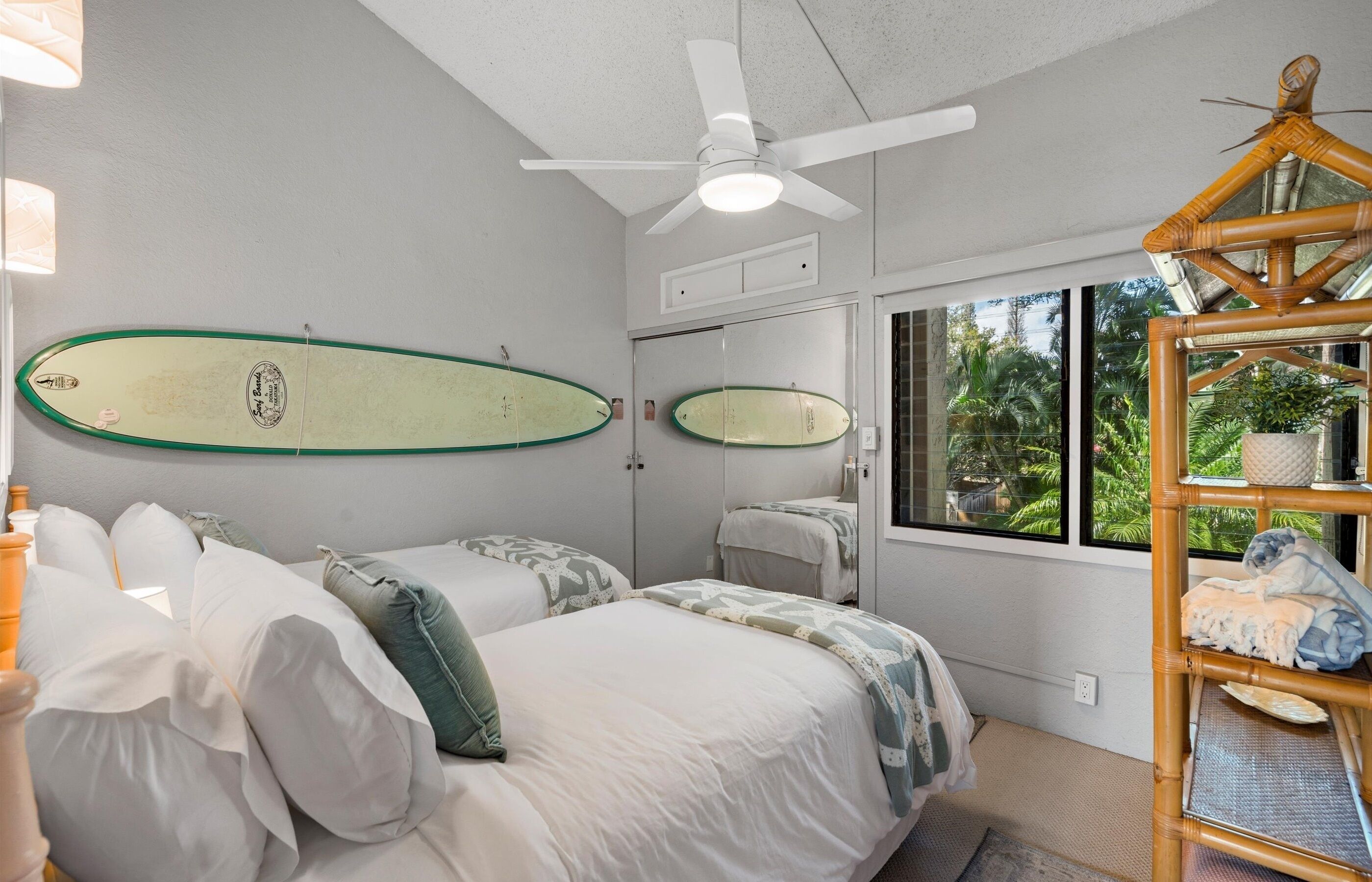 A bedroom with two beds, a ceiling fan, and surfboards on the wall.