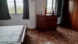 Een slaapkamer met een bed, een houten dressoir, een klok en een raam met gordijnen.