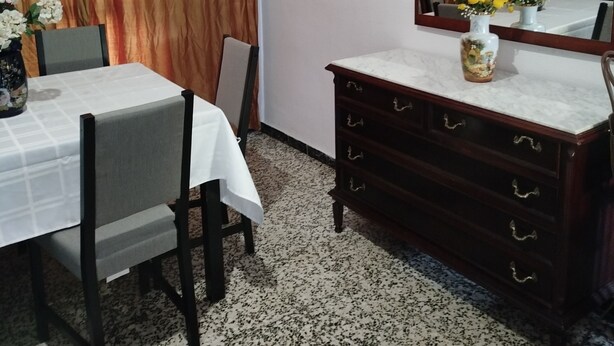 Een eetgedeelte met een tafel, stoelen, een houten dressoir en een spiegel.