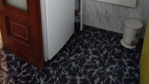 Een compacte keuken met een koelkast, een houten deur, een wit kastje en een vloer met een patroon.