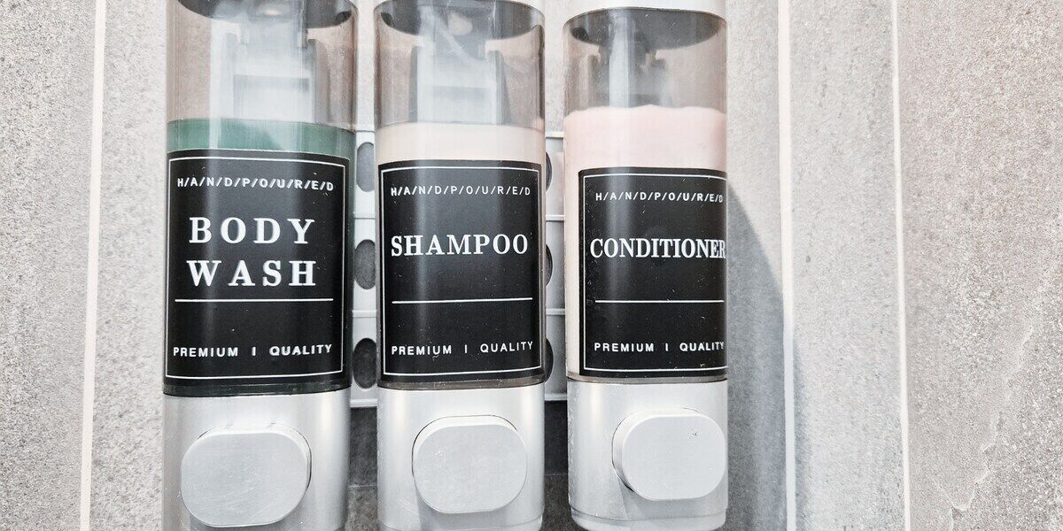 Trois flacons de gel douche, de shampoing et d’après-shampoing, présentés dans une salle de bain.