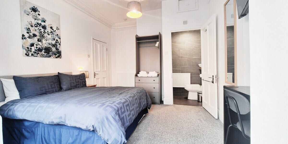 Une chambre comprenant un lit, une armoire, une salle de bain avec des toilettes et un lavabo, ainsi qu’un miroir.