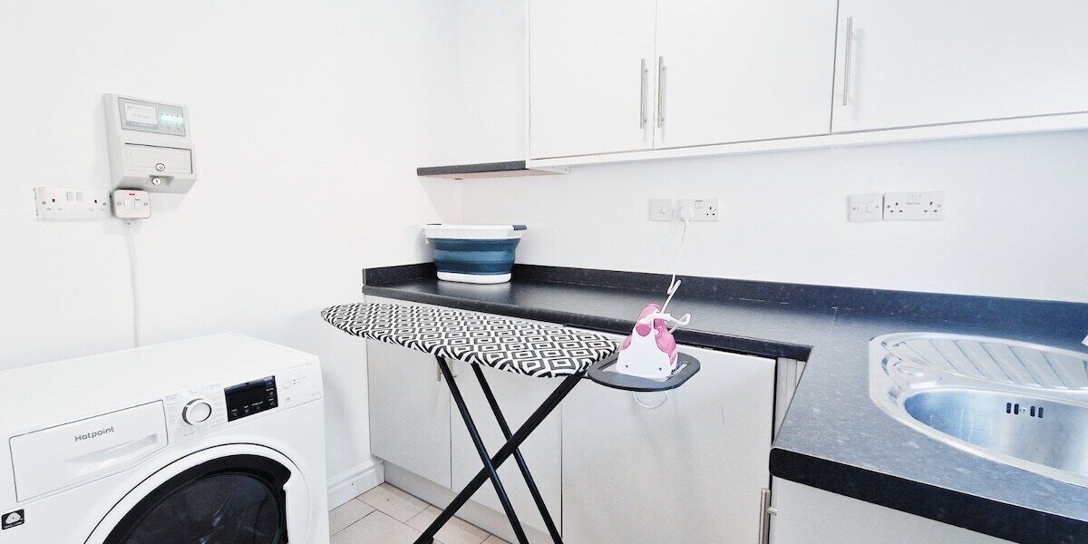 Cozinha compacta com máquina de lavar, tábua de passar roupa pequena, pia e micro-ondas.