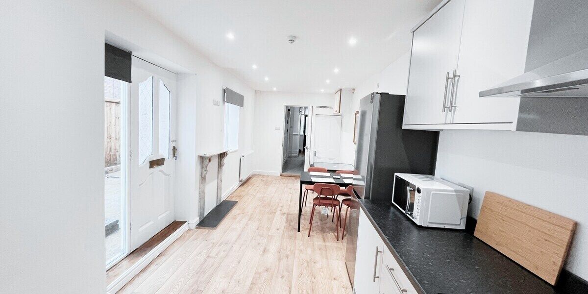 Een moderne keuken met witte kasten, een zwart aanrecht en een eethoek met een tafel en stoelen.