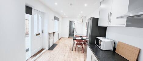 Een moderne keuken met witte kasten, een zwart aanrecht en een eethoek met een tafel en stoelen.