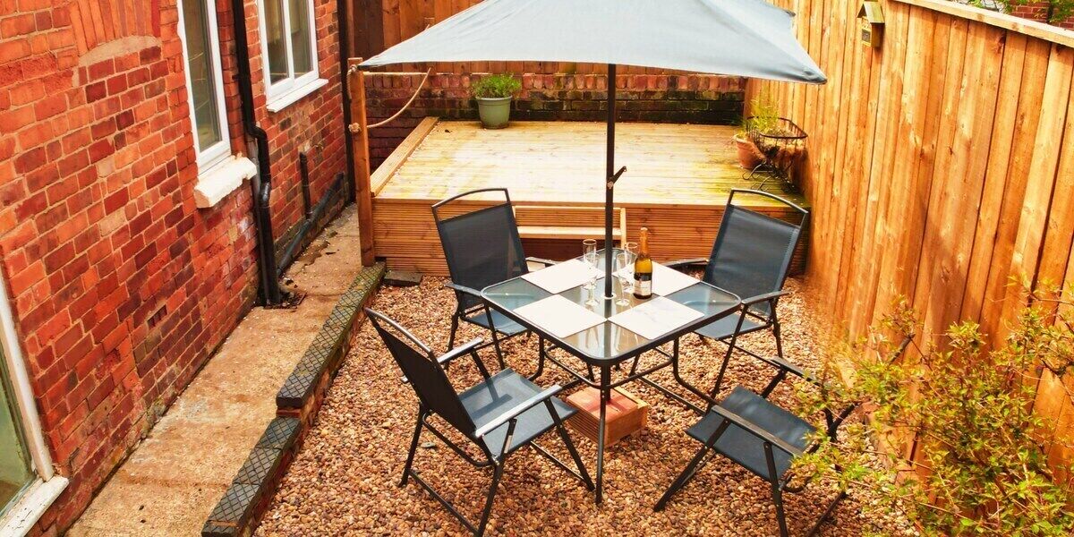A patio with a table and chairs, a wooden deck, and a brick wall.
