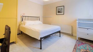 A bedroom with a bed, a radiator, a white dresser, and a yellow wardrobe.
