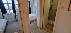 Habitació d'hotel amb un llit, una taula de nit, una petita còmoda i una zona de banyera/dutxa.