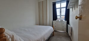 A small, simple bedroom with a single bed, a bedside table, a dresser, and a window with curtains. - Waterfront 2BD Flat with Balcony, Central Dublin (Dublin)