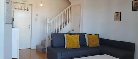 A living room with a dark grey sofa, two yellow cushions, a white coffee table, and a staircase with a white railing.
